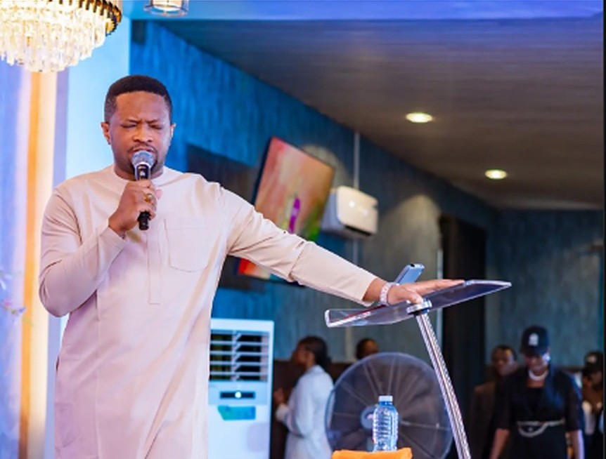 Pastor Godswill Oyor ministering beside a glass pulpit